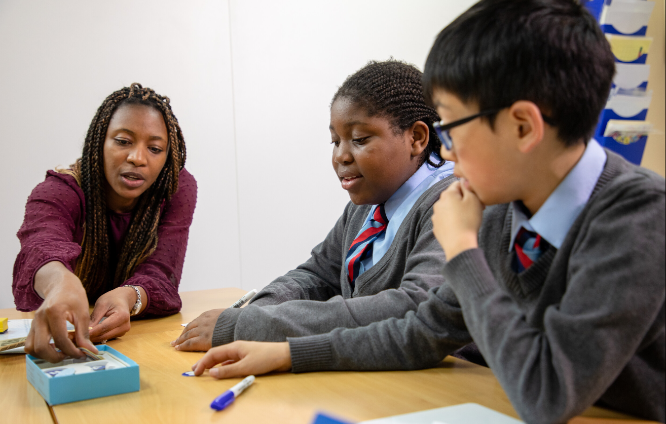 A teacher working through an exercise with two pupils in school uniform at a classroom table